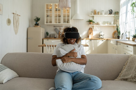 Surprised African American woman hugging pillow in virtual glasses watching movie, playing games