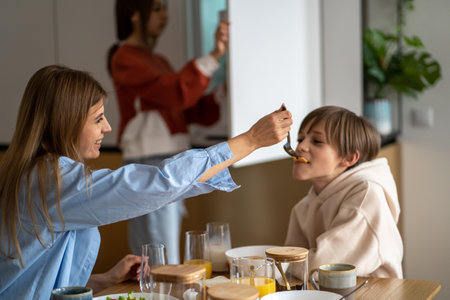 Happy mother feeding child son and smiling, mom and kid having fun while having breakfast togetherの写真素材