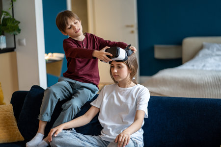 Caring small brother help curious teenage girl put on virtual reality glasses for immersive in game