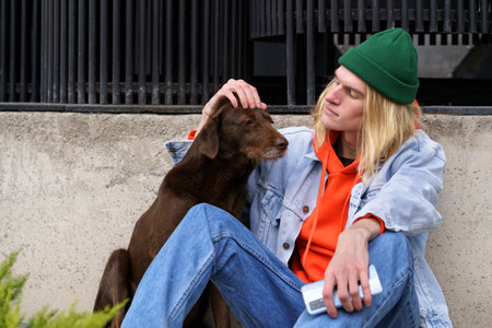 Hipster guy sitting on street with upset stray dog, problem of homeless animalsの写真素材