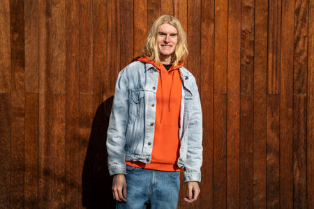 Happy positive millennial hipster guy with long blonde hair standing outdoors smiling at camera