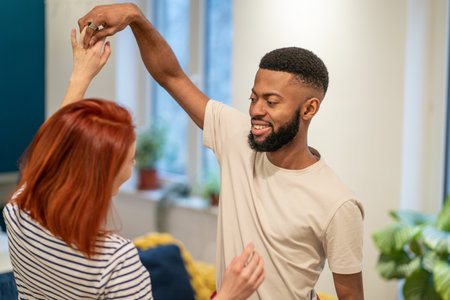 Happy romantic multiracial young couple in love learning to dance together at homeの写真素材