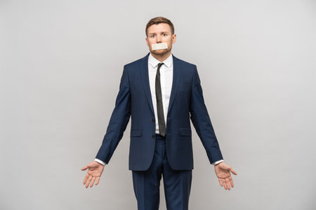 Upset desperate man with mouth sealed in concept of freedom of speech isolated on studio backgroundの写真素材