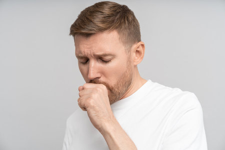 Sick man with flu symptoms feels discomfort coughs due to illness isolated on grey studio background