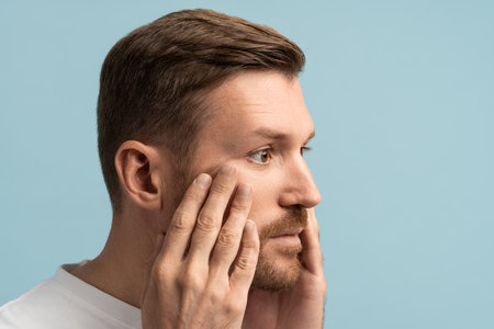Portrait of bearded sad middle aged man touching face skin having anxiety about aging process.の写真素材