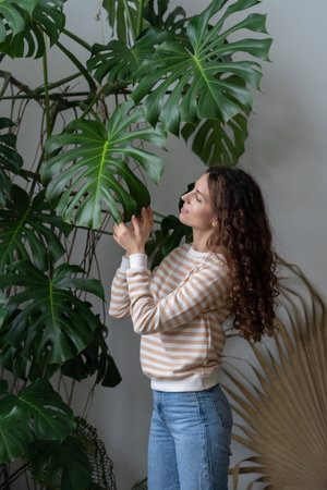 Young smiling woman touching Monstera plant leaf, enjoying home gardening and plantcareの写真素材