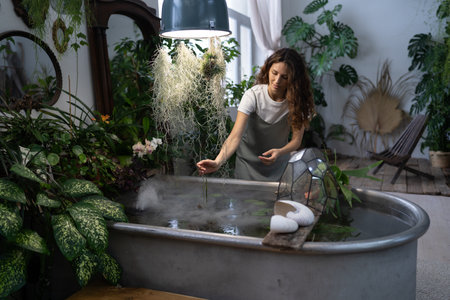 Girl gardener taking care about aquatic plant in greenhouse holding houseplant under bath with waterの写真素材