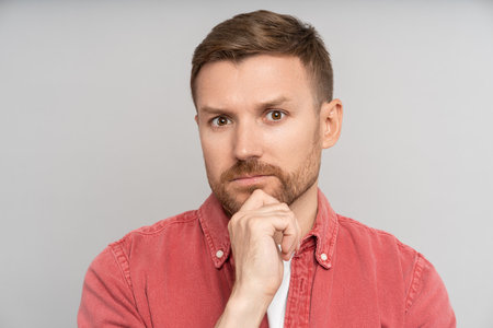 Puzzled thoughtful pensive man looking at camera touching chin feeling doubts isolated background.の写真素材