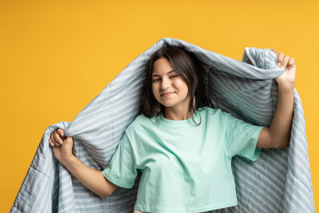 Brunette positive woman covering in grey blanket on yellow background looking at camera.の写真素材