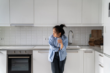 Unhappy Asian woman suffers from pain in stomach or menstruation ache drinking painkiller with waterの写真素材