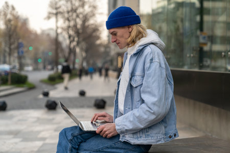 Concentrated self-sufficient man with laptop sits near building works as programmer in IT companyの写真素材