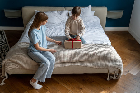 Mother sitting on bed with little boy child opening wrapped gift boxの写真素材