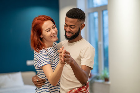 Joyful young diverse married couple dancing having fun in living room at homeの写真素材