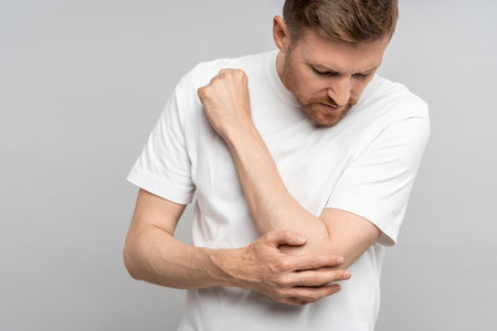 Middle aged man touching hand elbow feeling pain isolated on gray background after injury.の写真素材