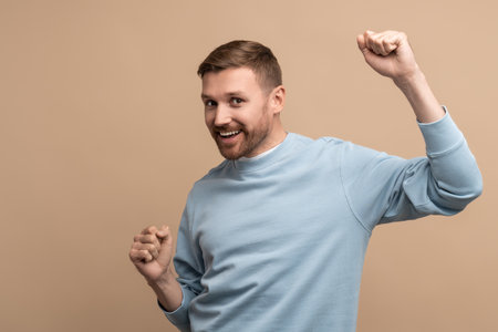 Overjoyed happy man showing win victory gesture on beige background looking at camera.の写真素材