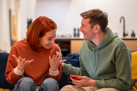 Happy overjoyed couple man woman reading good news in smartphone sitting on couch at home.