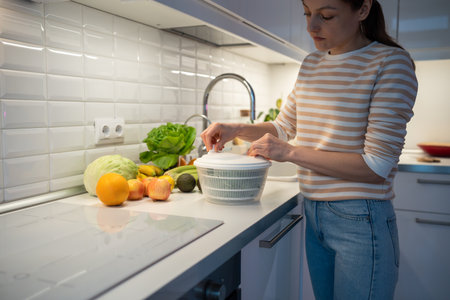 Slender female on diet cooking quick fresh healthy salad by drying greenery in hand food centrifuge.の写真素材