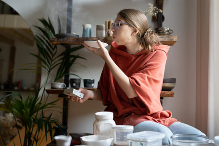 Master potter woman blows off dust after cleaned handmade clay product. From hobby to small business