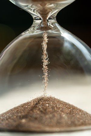 Shiny sand grains running in inverted hourglass lasting certain amount of time as transience of lifeの写真素材