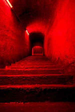 Dark eerie staircase leading to underground space illuminated by red neon light, mysterious tunnelの写真素材