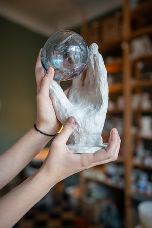 Glass ball rests in handcrafted clay hand decor in ceramist hands. Glassmaking and pottery as artの写真素材
