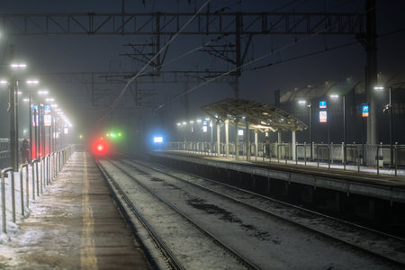 Dense fog covers train station platform with faint halo of lights on empty illuminated stationの写真素材