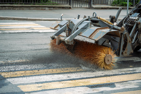 Tractor sweeps gravel from road after repair work at pedestrian cross. City renovation, maintenanceの写真素材