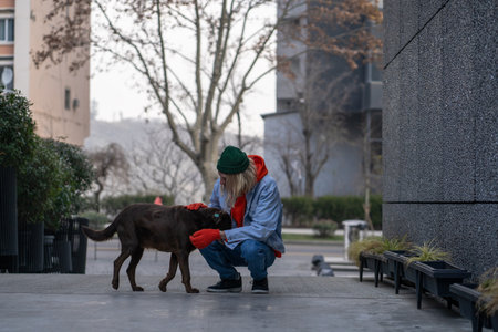 Kind, warm-hearted stylish guy in trendy outfit sitting on haunches, caressing hungry street dogの写真素材
