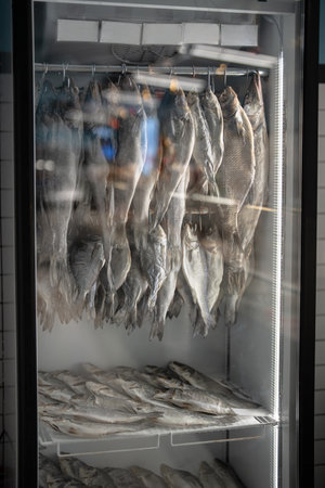 Dried salted fish snacks selling in local fishmonger, stored in big refrigerator with price tags.