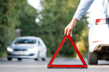 man driver putting red warning triangle - emergency stop sign behind his broken car