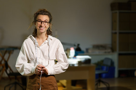 Young self-employed woman tailor business owner. Happy seamstress with measuring tape in atelierの写真素材