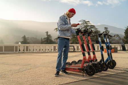 Young man tourist trying to unlock e-scooter with mobile app, exploring city on electric scooter