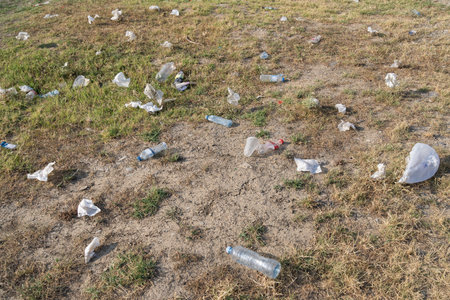 Scattered plastic bottles and bags lie on grass in rural area causing pollution of environmentの写真素材