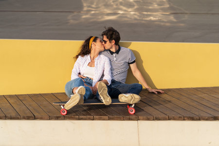 Trendy couple of skaters sit on longboard kissing. Romantic date of millennial hipsters outdoorsの写真素材