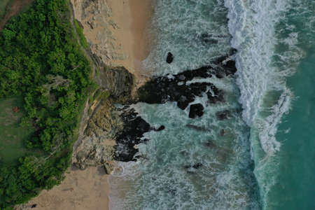 Aerial image of Uluwatu Temple, ocean and wave breaking on rocks on the beach near cliff. Bali,...