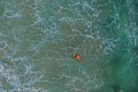 Aerial image of girl swimming on a surfboard in the blue Indian ocean, Dreamland beach, Bali,...