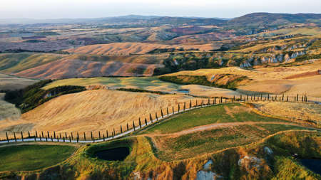 Aerial view of Tuscany region at sunset. Val dâOrcia, Italy. Golden and green glades, road with cypress trees, hills, small pond, tuscan villa.の写真素材