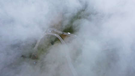 Aerial view of winding road with driving cars through clouds from above. Dolomites, South Tyrol,...
