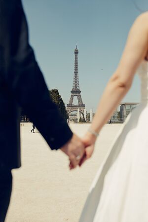 bride and groom keep their hands on the Eiffel Tower backgroundの写真素材