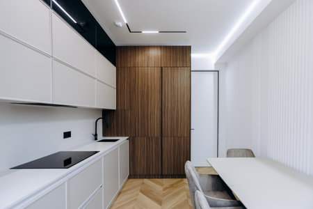 A kitchen with white cabinets, stove top oven, table and chairsの写真素材