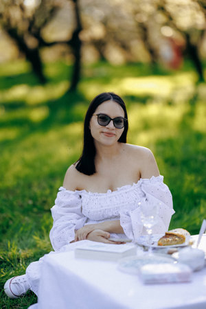 A woman in a flowing white dress sits peacefully at a grass tableの写真素材