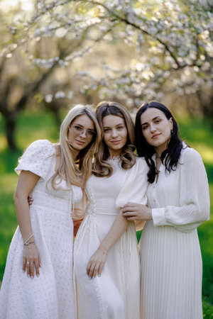 Three women in white dresses pose by a cherry blossom treeの写真素材