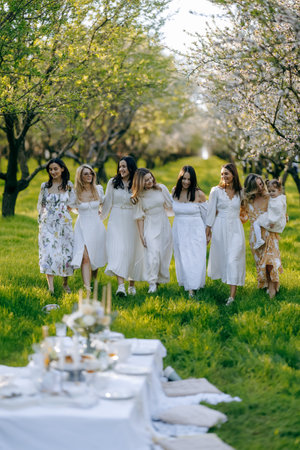 Women in elegant white dresses walk gracefully in a parkの写真素材