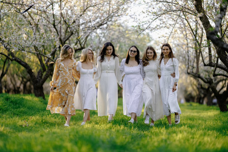 A group of women in elegant white dresses walks joyfully in springの写真素材