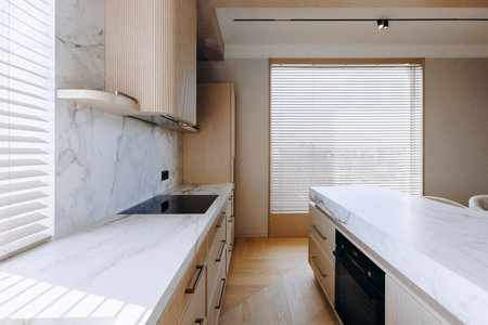 A kitchen with white countertops, wooden cabinets, a sink, and a windowの写真素材