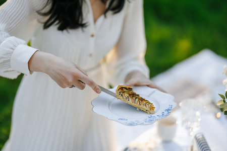 A woman is carefully cutting a slice of pie that is on a plateの写真素材