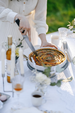A woman is carefully cutting a delicious pie on a table surfaceの写真素材