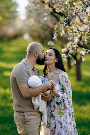A man kisses a woman on the cheek while holding a baby in a parkの写真素材