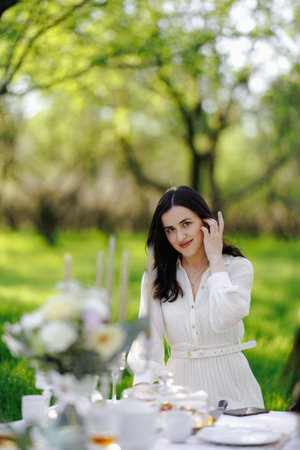 A woman in a beautiful white dress sits at a table in a parkの写真素材