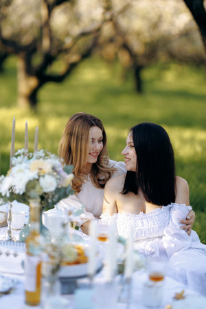 Two women sit at a table in the grass, looking at each otherの写真素材